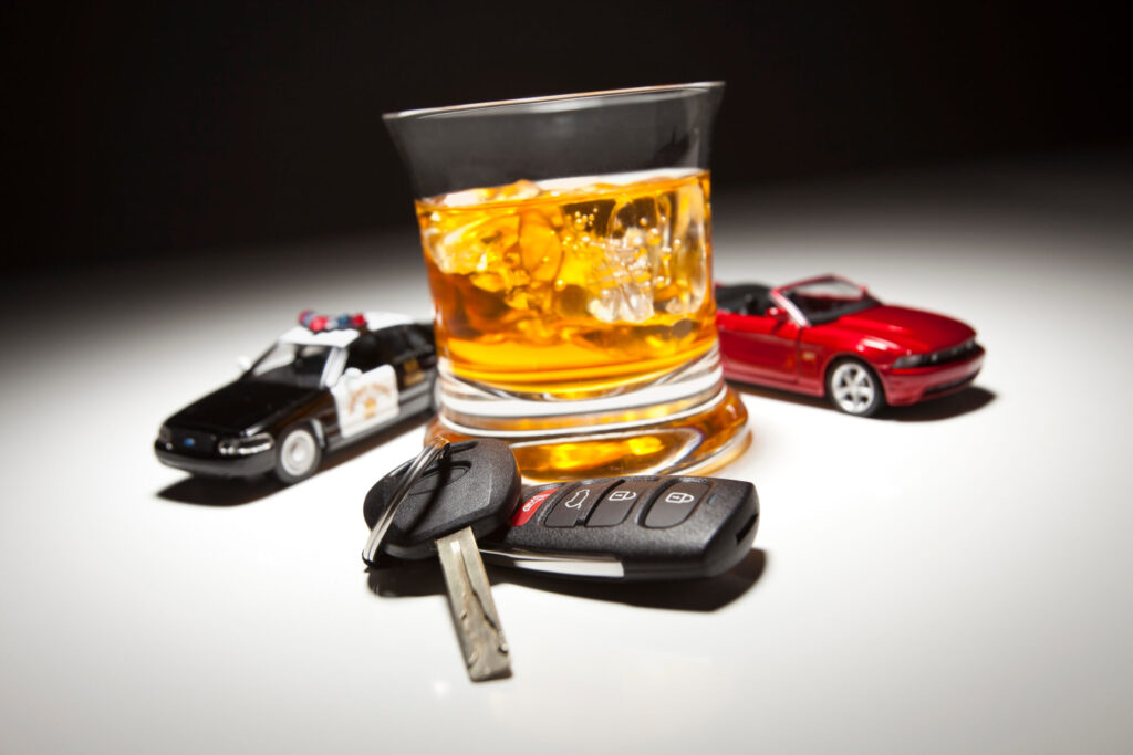 Glass of whiskey with ice, car keys, and toy police and sports cars, symbolizing the consequences of DUI offenses.