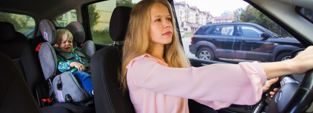 Female driver focused on steering while a toddler in a car seat looks on, emphasizing the risks of DWI with a minor passenger in Texas.