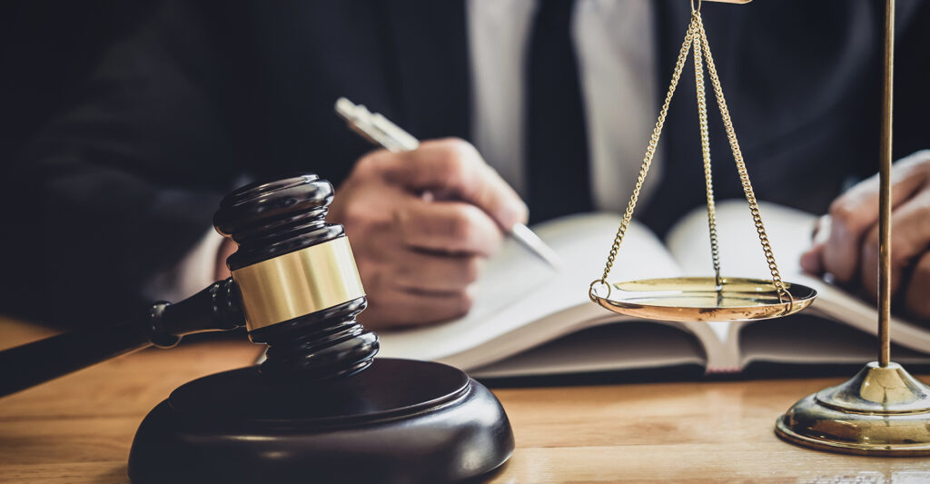 Gavel and scales of justice on a desk with a lawyer writing notes, symbolizing legal advice for DUI cases.