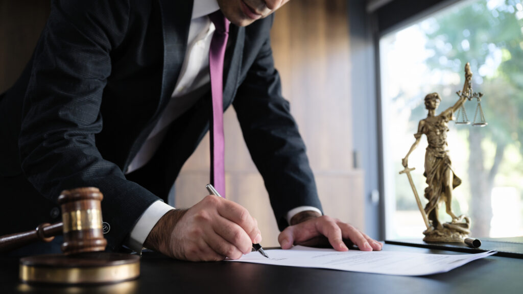 Lawyer in a suit signing documents at a desk with a gavel and a Lady Justice statue, symbolizing legal representation in Texas misdemeanor cases.