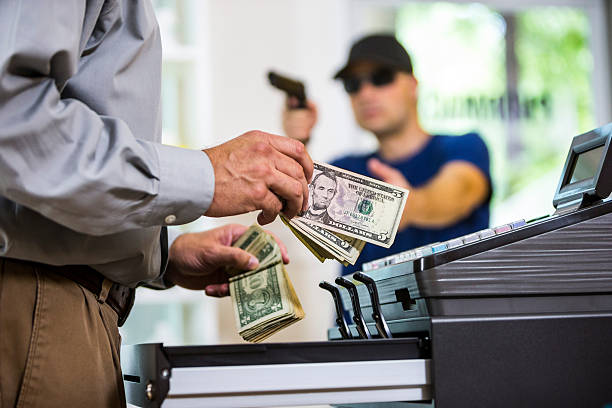 Man handing cash to a register while an armed robber in sunglasses threatens from behind, illustrating a robbery scenario relevant to Texas aggravated robbery laws.