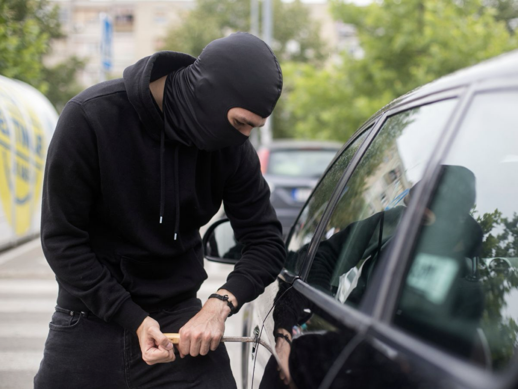 Masked individual attempting to break into a car, illustrating burglary in the context of Texas law and penalties.