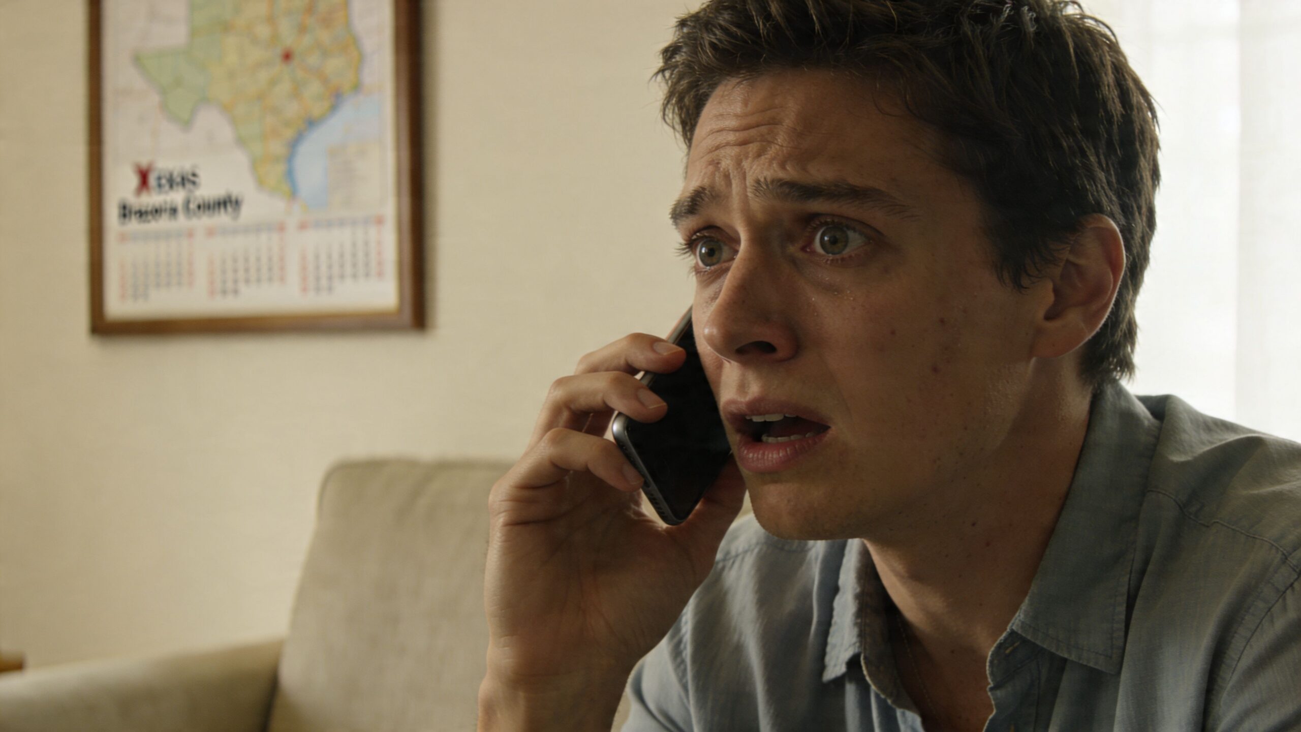 A distressed young man talking on his smartphone in an office with a map of Brazoria County